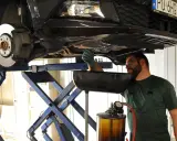 Mechanik w warsztacie wymienia zużyty olej samochodowy. Podniesiony pojazd i naczynie na płyn wskazują na rutynową czynność serwisową.