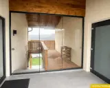 Moderner, verglaster Windfang aus Aluminium mit Holzbalken und Blick auf eine Holzterrasse.