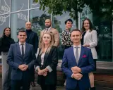 Grupa prawników w garniturach i eleganckich strojach stoi przed nowoczesnym budynkiem.