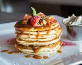 Pancakes con sciroppo d'acero, fragole e panna. Il dulcis in fundo significato di una colazione perfetta.