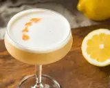 En läcker sifon drink med skummig topp, garnerad med orange mönster. Citroner och en jigger ligger bredvid.