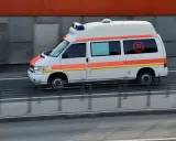 Biała karetka z pomarańczowymi pasami pędzi na sygnale. To pojazd uprzywilejowany, który może brać udział w kursie na pojazdy uprzywilejowane.