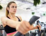 Junge Frau trainiert konzentriert auf einem Crosstrainer, um abzunehmen. Sie hört Musik über Kopfhörer.