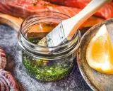 Marinade mit Kräutern und Zitrone bereit, um den Lachs zu verfeinern. Ein Pinsel liegt in der Glasflasche.