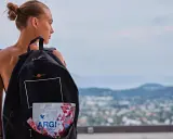 Młoda kobieta z plecakiem, w którym widać opakowanie ARGI+. W tle krajobraz miasta i wzgórz.