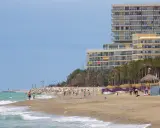 Menschen genießen den sonnigen torremolinos strand mit Palmen und einem großen Hotel im Hintergrund.