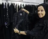 A woman smiles, holding a black lace abaya, showcasing elegant Saudi Arabia fashion.
