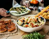 Pyszna sałatka makaronowa z oliwkami i pomidorkami, obok pieczywo i świeże oregano. Idealne na letni obiad, pokazujące co zrobić z oregano.