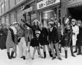 Ungdomar i trendiga kläder utanför en op-shop i Sverige 1960. Snö på marken och glada miner.
