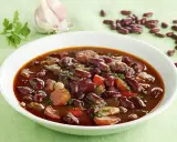 Un plato humeante de judías pintas con trozos de carne y verduras, decorado con perejil fresco.