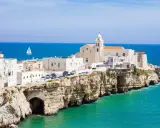 Un borgo bianco su scogliere a picco sul mare turchese, con una chiesa imponente. Un assaggio di cosa vedere in Puglia, con un veliero all'orizzonte.