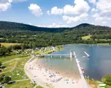Słoneczny dzień nad zalewem w Starej Morawie. Ludzie odpoczywają na plaży i w wodzie, a w tle widać zielone wzgórza.