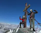 Dwóch alpinistów na szczycie najwyższego szczytu w Austrii. Widok na góry i chmury poniżej.