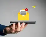 Dłoń trzyma smartfon, z którego wylatuje żółta koperta z powiadomieniem. Jak napisać SMSa o urlop na żądanie?