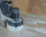 Bodenmaschine poliert Marmor. Staub und Wasser bilden Muster auf dem Boden, während die Maschine den Stein glänzend macht.