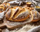 Une brioche au levain, mie filante, saupoudrée de farine, sur une planche en bois. Du beurre et de la confiture sont à proximité.