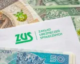 Koperta z logo ZUS leży na stosie polskich banknotów. z15b druk.