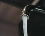 Un robinet chromé verse un jet d'eau. L'image évoque la dureté de l'eau par commune en France, un sujet important pour la vie quotidienne.