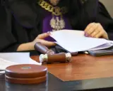 Sędzia w todze z orłem przegląda dokumenty. Na stole młotek i telefony. Sprawa spadkobiercy w toku.