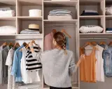 Kobieta porządkuje szafę, wieszając ubrania. Widać półki z poukładanymi rzeczami i wieszaki z odzieżą. To inspiracja, wie organisiert man den kleiderschrank.