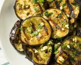 Aubergines grillées en rondelles, garnies d'ail et de persil, sur une assiette.