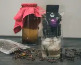 Napój z cascary, czyli co to jest kombucha z kawy, w szklance z lodem i słomką. Obok słoik z napojem i paczka z cascara.