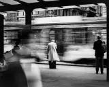 Street photography esempi: un tram sfreccia, lasciando figure sfocate in attesa alla fermata.