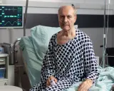 Starszy mężczyzna w szpitalnym łóżku, z tlenem w nosie, walczy z ostrą białaczką szpikową. Monitor pokazuje jego parametry życiowe.