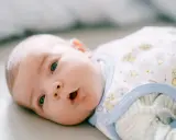 Niebieskie oczy noworodka otwierają się, by odkryć świat. Ubrany w pajacyk z misiami, patrzy z zaciekawieniem.