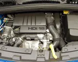 Silnik HDI 16 w Citroenie C4. Widoczny jest czarny plastikowy dekiel z napisem "HDI 16", przewody, rury dolotowe i inne elementy jednostki napędowej.