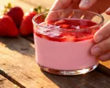 Délicieux panna cotta fraise, onctueux et fruité, servi dans un verre sur une table en bois. Des fraises fraîches sont disposées à côté.