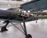 Ein altes Flugzeug, ein Storch, steht in einer Halle. Das Flugzeug hat eine Tarnlackierung und ein Kreuz auf dem Heck.