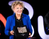 Una donna sorride sul palco, tenendo un premio a forma di libro aperto. Un simbolo di ispirazione per le libere donne.