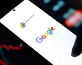 Ekran smartfona z logo Google i napisem Google Discover. W tle wykresy giełdowe.