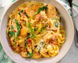 En skål med krämig pasta med soltorkade tomater, kyckling och spenat, toppad med riven parmesan och färska örter.