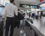 Resenärer på rullband på flygplatsen, skyltar visar vägen till gate F08-76. En man med resväskor på väg mot centrum.