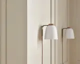 Dwa białe, prążkowane kinkiet z drewnianą nakładką, wiszące na jasnej ścianie.