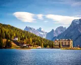 Lago alpino con hotel giallo e boschi autunnali, ideale tra i laghi da visitare in giornata.