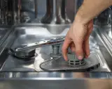 Main d'homme retirant le filtre du lave-vaisselle, une étape avant le nettoyage avec de l'acide citrique.