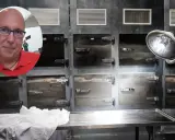 Mężczyzna w okularach i czerwonej koszulce na tle chłodni, gdzie odbywa się balsamacja.