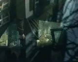 Mężczyzna w bluzie z zamkiem przy drzwiach samochodu, z ręką w kieszeni, na tle zniszczonej ściany. Scena sugeruje naruszenie miru domowego.