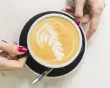 Une main tient une tasse de café latte avec un dessin de feuille. Un guide pour comment faire un latte parfait.