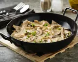 Herzhaftes geschnetzeltes mit Pilzen in cremiger Sauce, garniert mit Petersilie, serviert in einer schwarzen Pfanne.