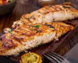 Två saftiga laxfiléer, perfekt grillade på halster, ligger på en träbricka. En citronskiva och rosmarinkvistar pryder fisken.