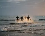 Vier Schwimmer stürmen ins Meer. Die durchschnittliche Zeit für 1km schwimmen wird hier wohl im Wettkampf ermittelt.