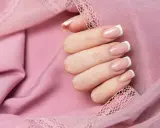 Eleganckie paznokcie na urodziny, w klasycznym stylu francuskim, na tle pudrowego różu z koronką.