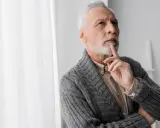 Uomo anziano con barba bianca, pensieroso, con un dito sul mento, forse valutando i risultati di un decadimento cognitivo test.