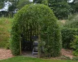 Un abri naturel formé par une **haie osier vivant**, avec des sièges et une table à l'intérieur, invitant à la détente.