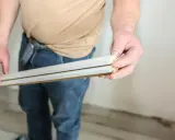 Ręce trzymają listwy styropianowe, które tworzą kąt rozwarty, gotowe do montażu.