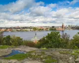 Vy över Riddarfjärden från Skinnarviksberget Stockholm, med Stadshuset i bakgrunden under en molnig himmel.